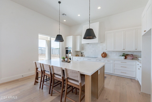 kitchen featuring an island with sink, light hardwood / wood-style floors, tasteful backsplash, and white cabinetry