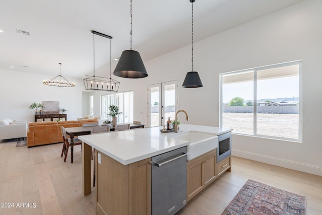 kitchen with light hardwood / wood-style floors, stainless steel appliances, hanging light fixtures, an island with sink, and sink