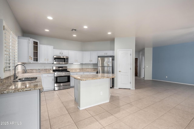 kitchen with sink, a center island, stainless steel appliances, light stone countertops, and white cabinets