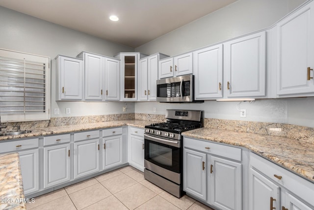 kitchen with light stone countertops, appliances with stainless steel finishes, light tile patterned floors, and white cabinets