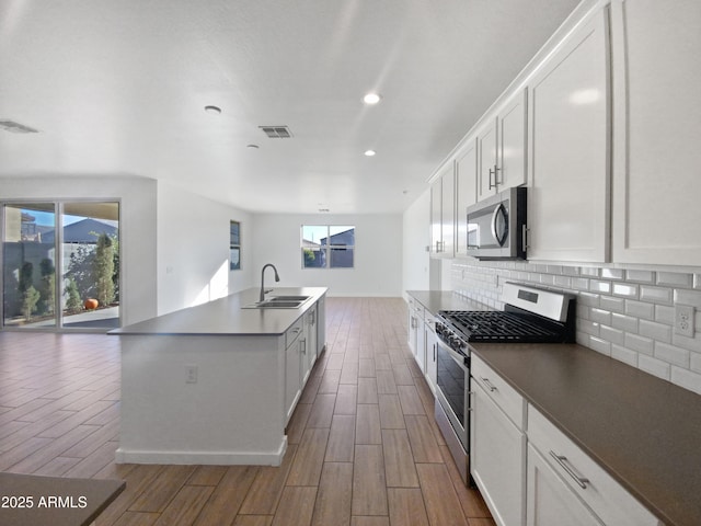 kitchen with appliances with stainless steel finishes, an island with sink, white cabinetry, and sink