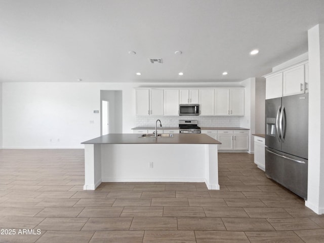 kitchen featuring white cabinetry, stainless steel appliances, decorative backsplash, a kitchen island with sink, and sink