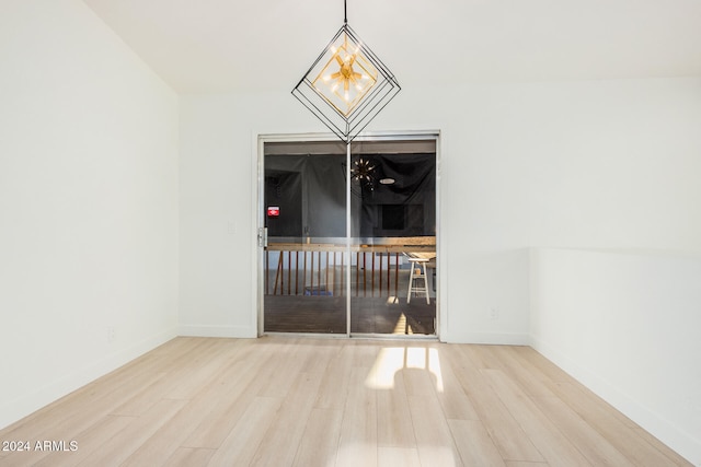 empty room with wood-type flooring and an inviting chandelier