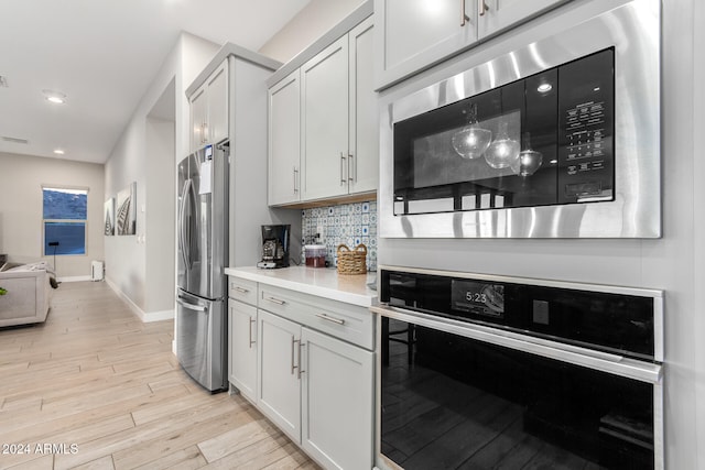 kitchen with white cabinets, stainless steel appliances, backsplash, and light hardwood / wood-style flooring