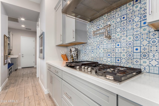 kitchen featuring white cabinetry, backsplash, wall chimney range hood, stainless steel gas cooktop, and light hardwood / wood-style flooring