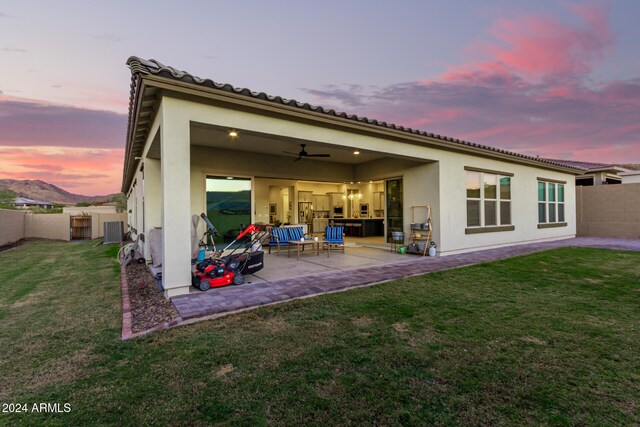 back house at dusk with ceiling fan, a lawn, and a patio area