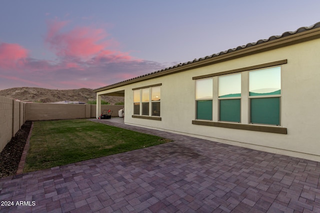 back house at dusk featuring a lawn, a mountain view, and a patio