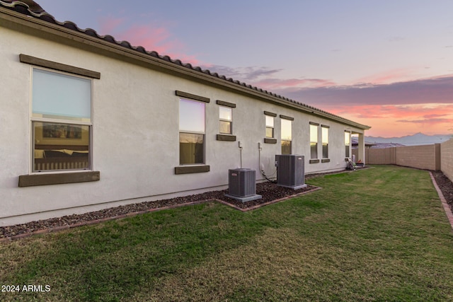 back house at dusk with central AC and a yard