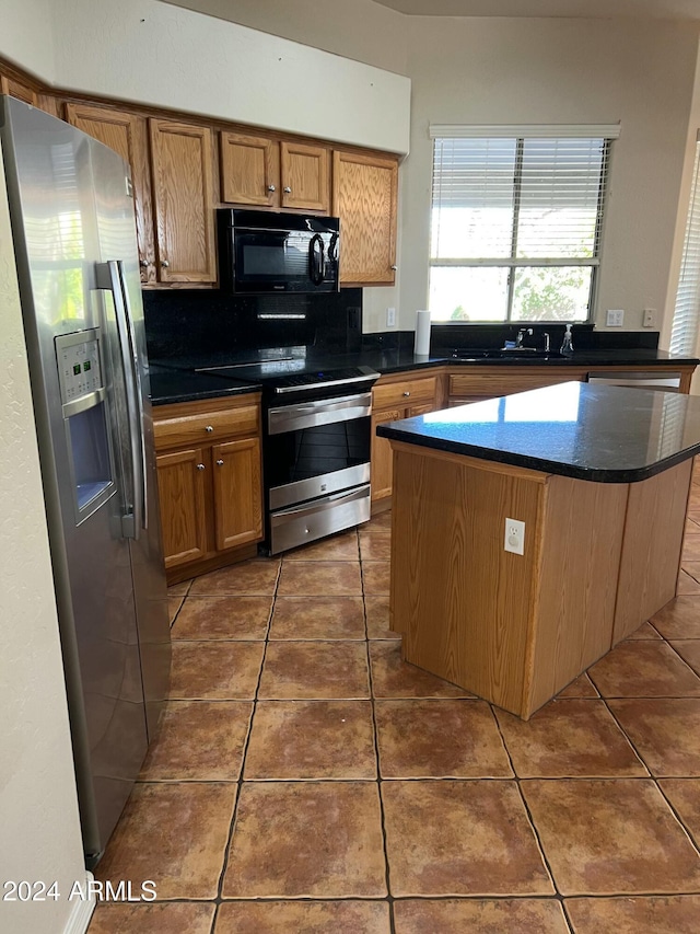 kitchen with dark tile patterned floors, a kitchen island, stainless steel appliances, and sink