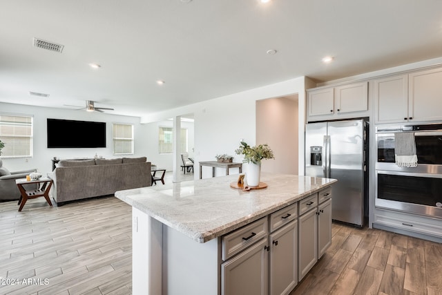 kitchen featuring light stone counters, appliances with stainless steel finishes, gray cabinetry, light hardwood / wood-style floors, and a center island