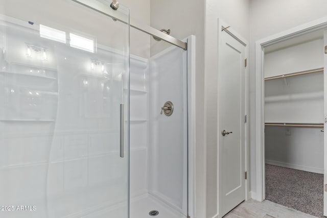 bathroom featuring a walk in closet, a shower stall, and baseboards