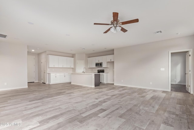 unfurnished living room featuring a sink, visible vents, light wood-type flooring, and baseboards