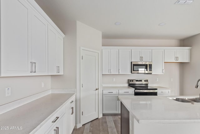 kitchen with light wood finished floors, a sink, light countertops, appliances with stainless steel finishes, and white cabinetry