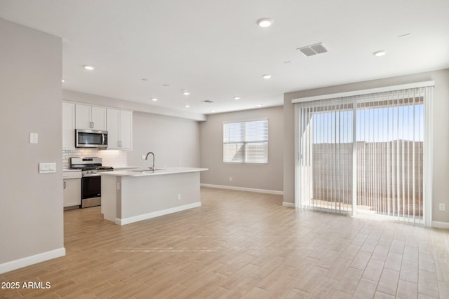 kitchen featuring a kitchen island with sink, white cabinets, sink, light hardwood / wood-style flooring, and appliances with stainless steel finishes