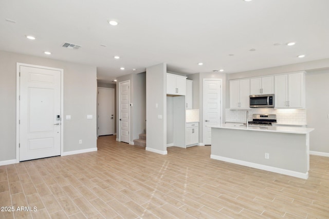 kitchen with tasteful backsplash, light hardwood / wood-style flooring, a kitchen island with sink, white cabinets, and appliances with stainless steel finishes