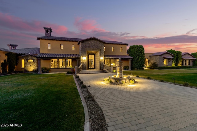 mediterranean / spanish house featuring stone siding, a front yard, decorative driveway, and stucco siding