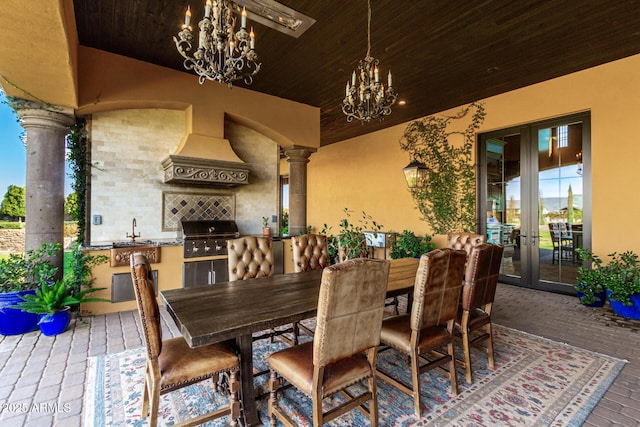 dining room featuring brick floor, a notable chandelier, wood ceiling, french doors, and decorative columns