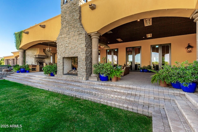 entrance to property with an outdoor stone fireplace, a patio, and stucco siding