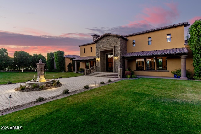 back of property featuring stone siding, a yard, decorative driveway, and stucco siding