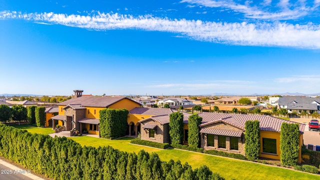 view of front of property featuring a tile roof, stucco siding, a front yard, a residential view, and stone siding