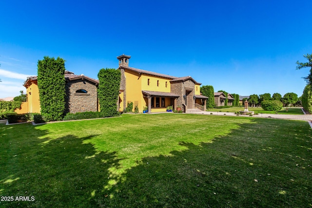 back of property featuring stone siding, a yard, a tile roof, and stucco siding