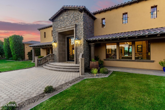 view of front of home featuring stone siding, a tile roof, a front lawn, and stucco siding