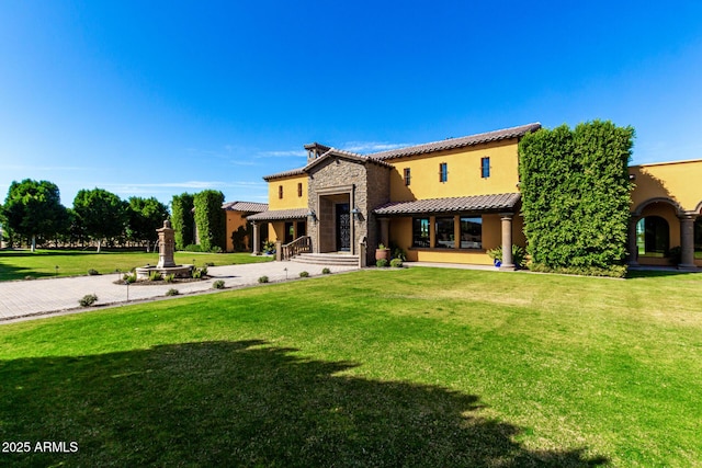 rear view of property featuring driveway, a lawn, stone siding, a tiled roof, and stucco siding