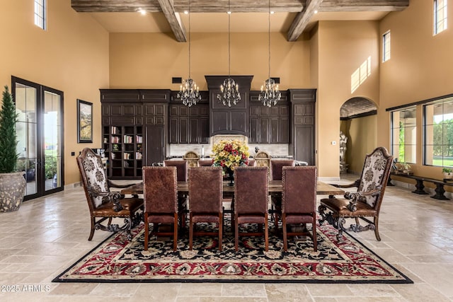 dining area featuring baseboards, a notable chandelier, a high ceiling, stone tile flooring, and beam ceiling