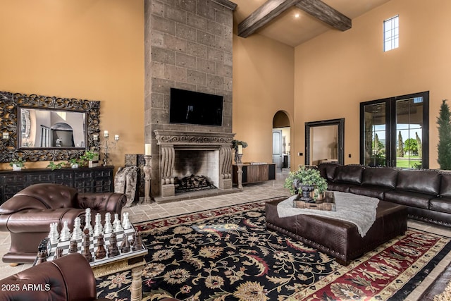 living area with arched walkways, a fireplace, a towering ceiling, and beamed ceiling