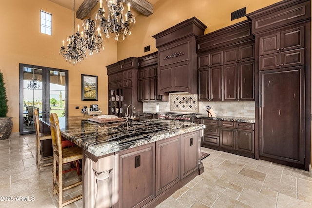 kitchen with a spacious island, dark stone countertops, stone tile flooring, a kitchen bar, and pendant lighting