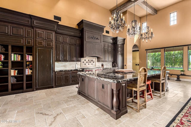 kitchen with pendant lighting, a spacious island, stone tile flooring, dark brown cabinetry, and a kitchen breakfast bar