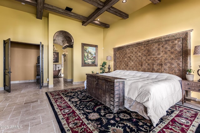 bedroom featuring arched walkways, recessed lighting, stone tile floors, baseboards, and beam ceiling