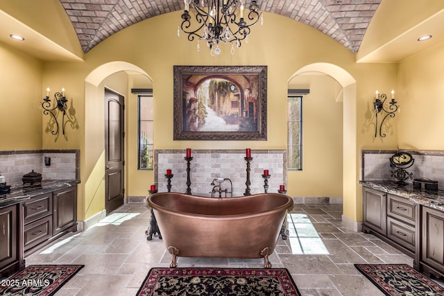 bathroom featuring stone tile flooring, a soaking tub, vaulted ceiling, brick ceiling, and baseboards