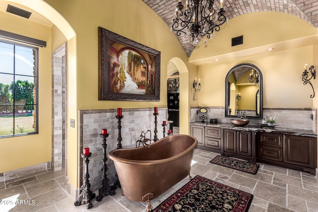 full bath featuring lofted ceiling, stone tile floors, visible vents, and a freestanding bath