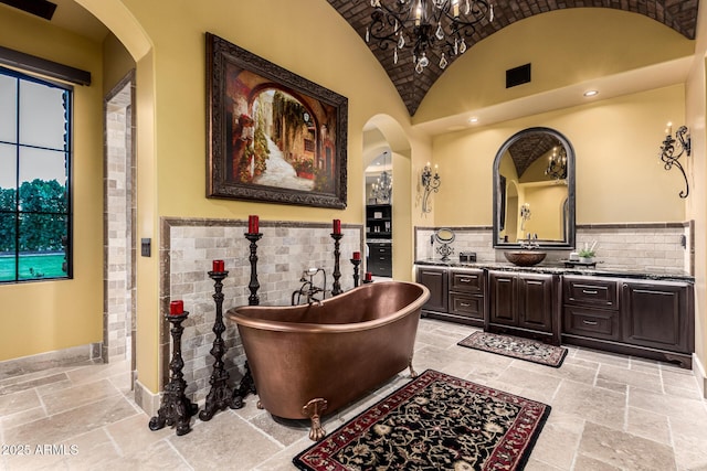 full bath featuring stone tile floors, baseboards, vaulted ceiling, vanity, and a freestanding tub