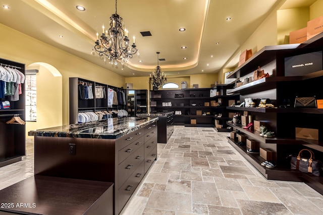 kitchen featuring arched walkways, dark stone counters, a spacious island, an inviting chandelier, and a tray ceiling