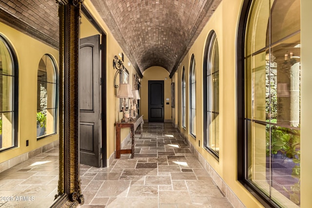 corridor with brick ceiling, stone tile floors, lofted ceiling, and baseboards