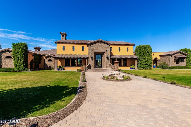 mediterranean / spanish-style house featuring stone siding, a tiled roof, decorative driveway, stucco siding, and a front lawn