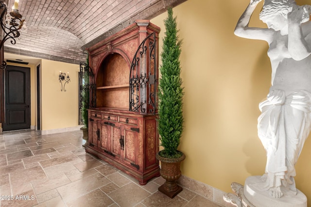 corridor with brick ceiling, baseboards, vaulted ceiling, and stone tile flooring