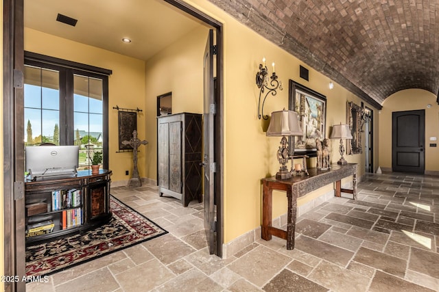 hallway with brick ceiling, stone tile floors, vaulted ceiling, and baseboards