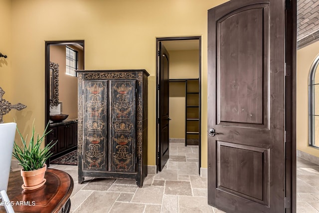 bathroom featuring baseboards, a walk in closet, and stone tile flooring