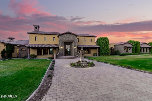 mediterranean / spanish home with decorative driveway, stone siding, a lawn, and stucco siding