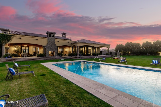 pool at dusk with a yard, an outdoor pool, and a patio