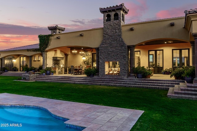 back of house at dusk featuring a yard, a patio, an outdoor kitchen, and stucco siding