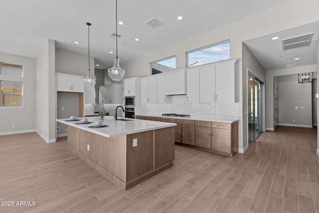 kitchen featuring light wood-type flooring, visible vents, light countertops, and backsplash