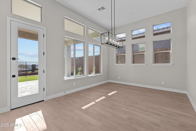 unfurnished dining area featuring a notable chandelier, baseboards, visible vents, and wood finished floors