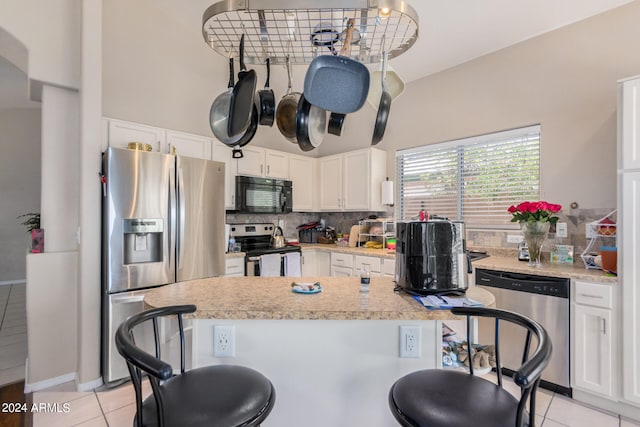 kitchen featuring white cabinets, tasteful backsplash, a breakfast bar area, appliances with stainless steel finishes, and light tile patterned flooring