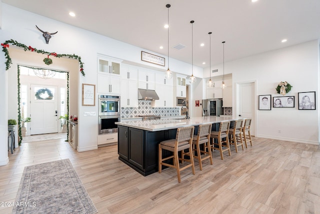 kitchen with light countertops, glass insert cabinets, white cabinetry, a large island with sink, and under cabinet range hood