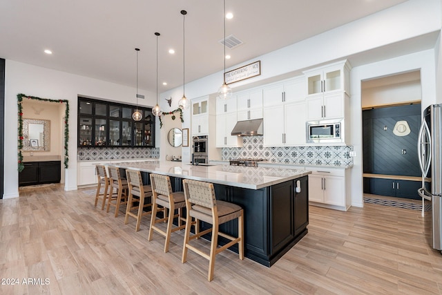 kitchen featuring visible vents, a spacious island, appliances with stainless steel finishes, decorative light fixtures, and under cabinet range hood