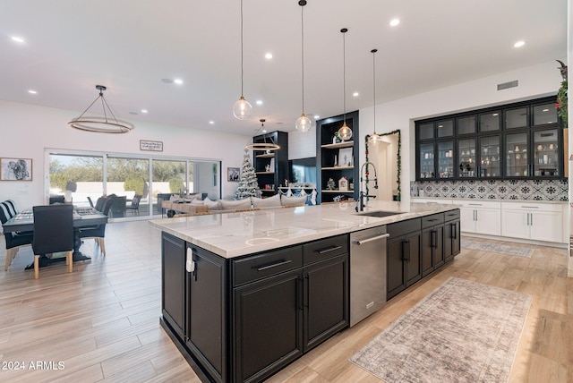 kitchen with decorative light fixtures, glass insert cabinets, open floor plan, a sink, and a large island with sink